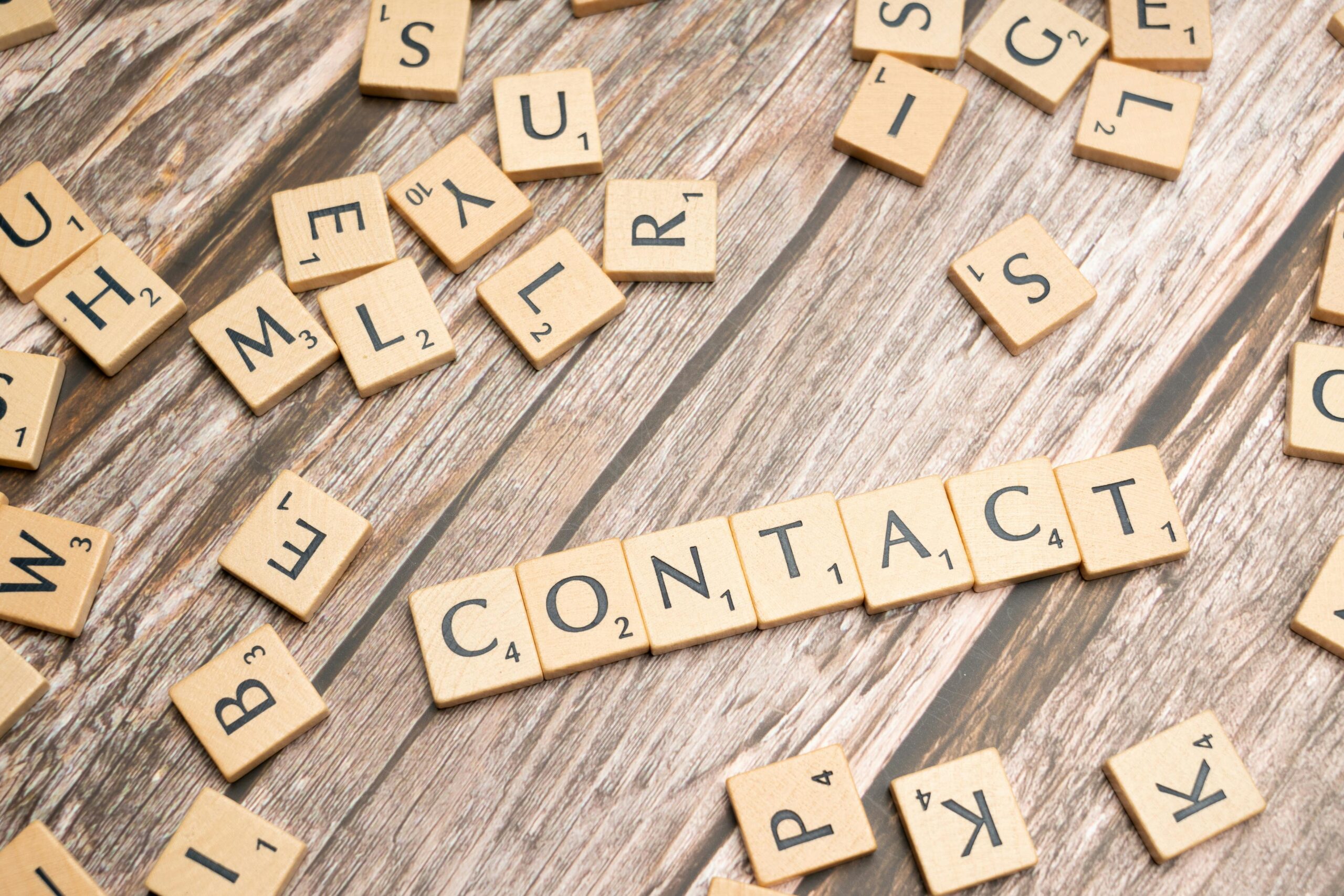 Scrabble-style letter tiles spelling 'contact' on wooden surface.